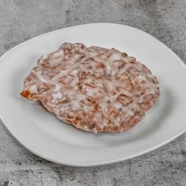 Dat Donut's apple fritter, generously covered in a sweet white glaze, on a white plate.