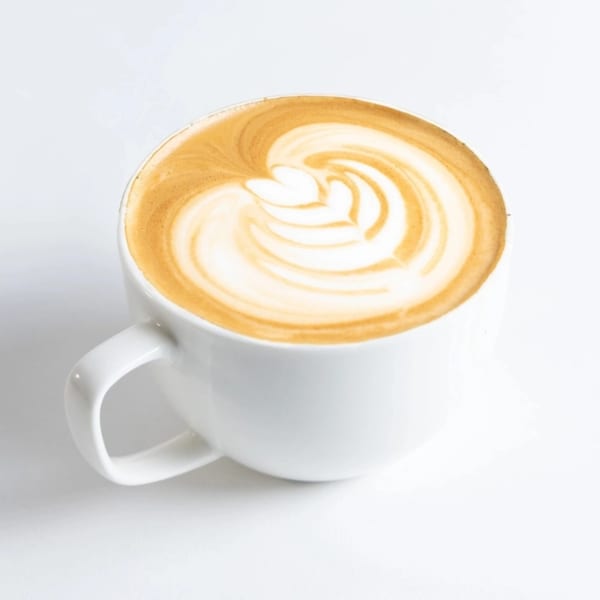 A white mug filled with a latte, featuring intricate latte art on top.
