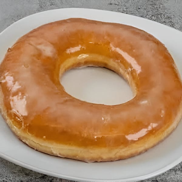 A single glazed Dat Donut on a white plate, showcasing its shiny, golden-brown coating.