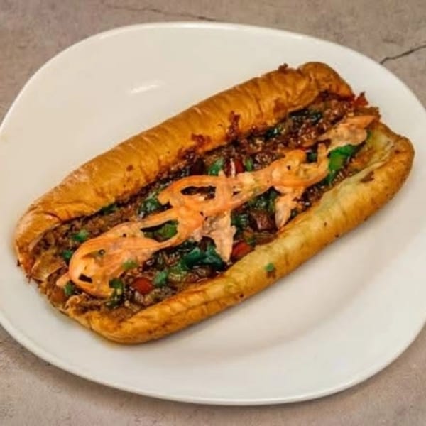 A long, golden-brown sandwich filled with meat, green herbs, and orange slices on a white plate.