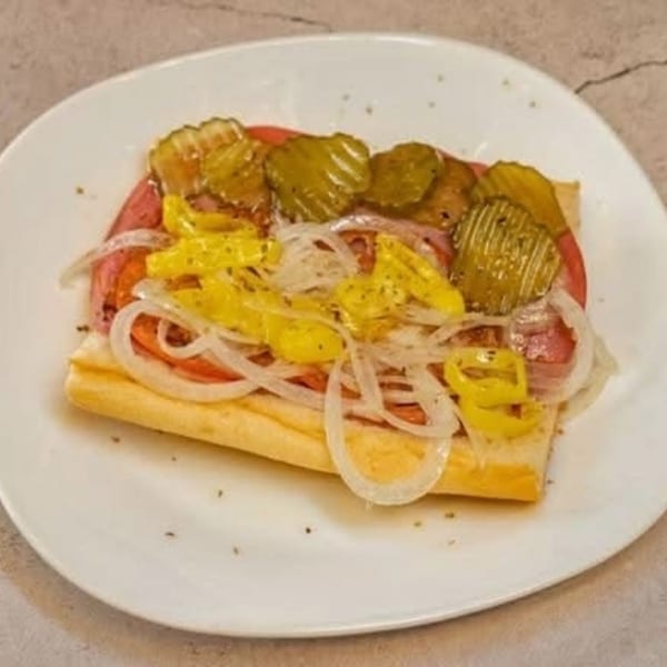 A submarine sandwich with meat, onions, pickles, and yellow peppers on a white plate.