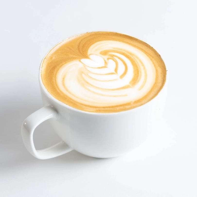 A white mug filled with a latte, featuring intricate latte art on top.