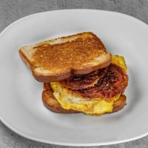 A breakfast sandwich with toasted bread, fried eggs, and bacon on a white plate.